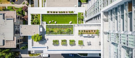 An aerial view of a modern building with a rooftop garden, multiple terraces, and a parking area.