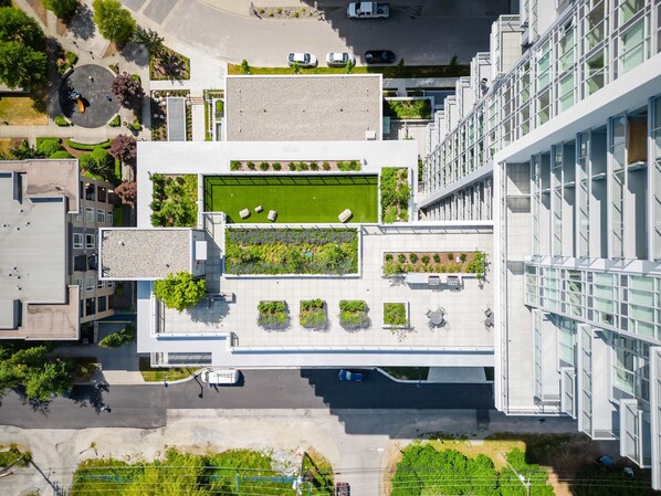 An aerial view of a modern building with a rooftop garden, multiple terraces, and a parking area. - Modern 2 Bed 2 Bath Condo with Parking, Patio & Amenities – Prime Location (Surrey)