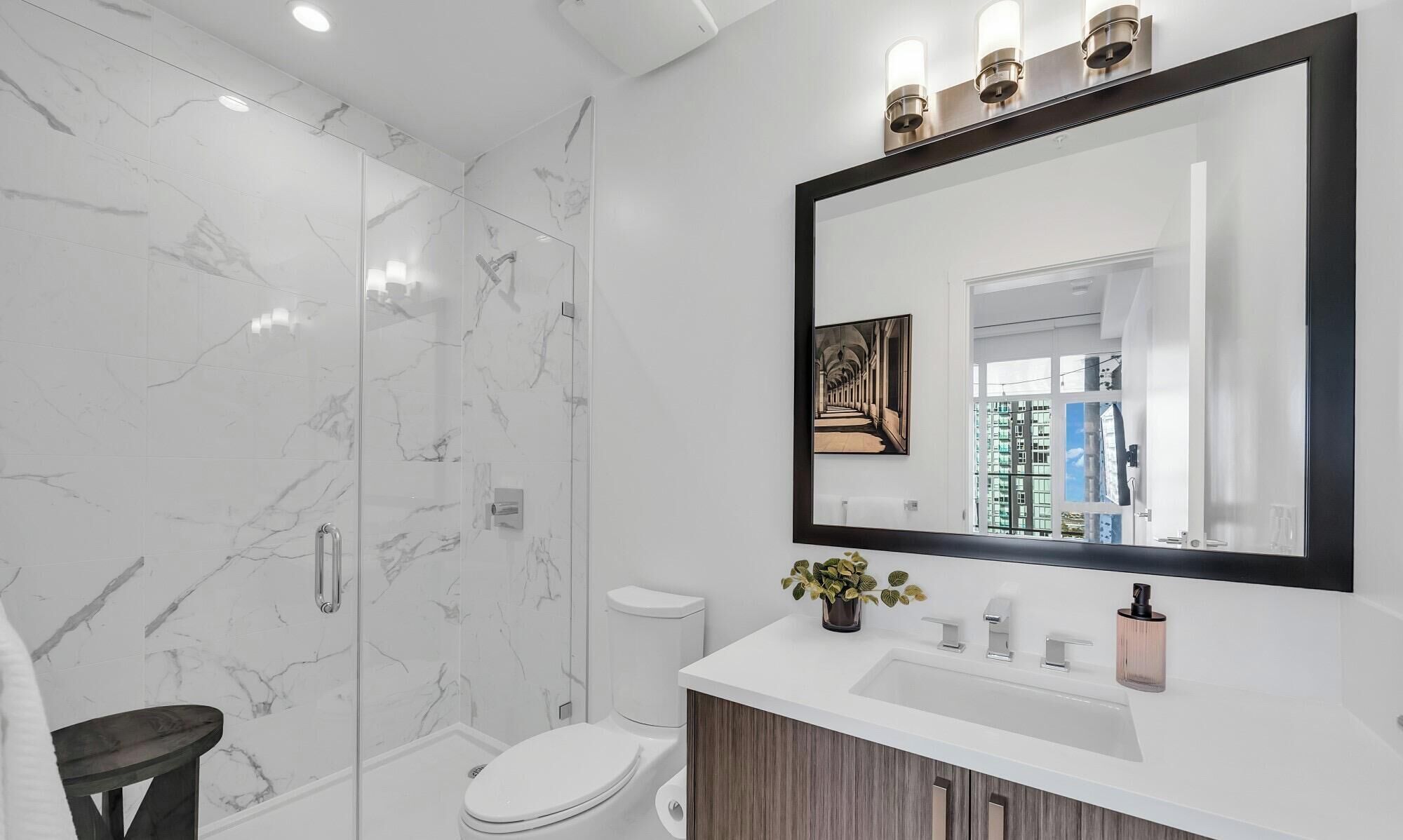 A modern bathroom with a large mirror, marble walls, and a wooden vanity.