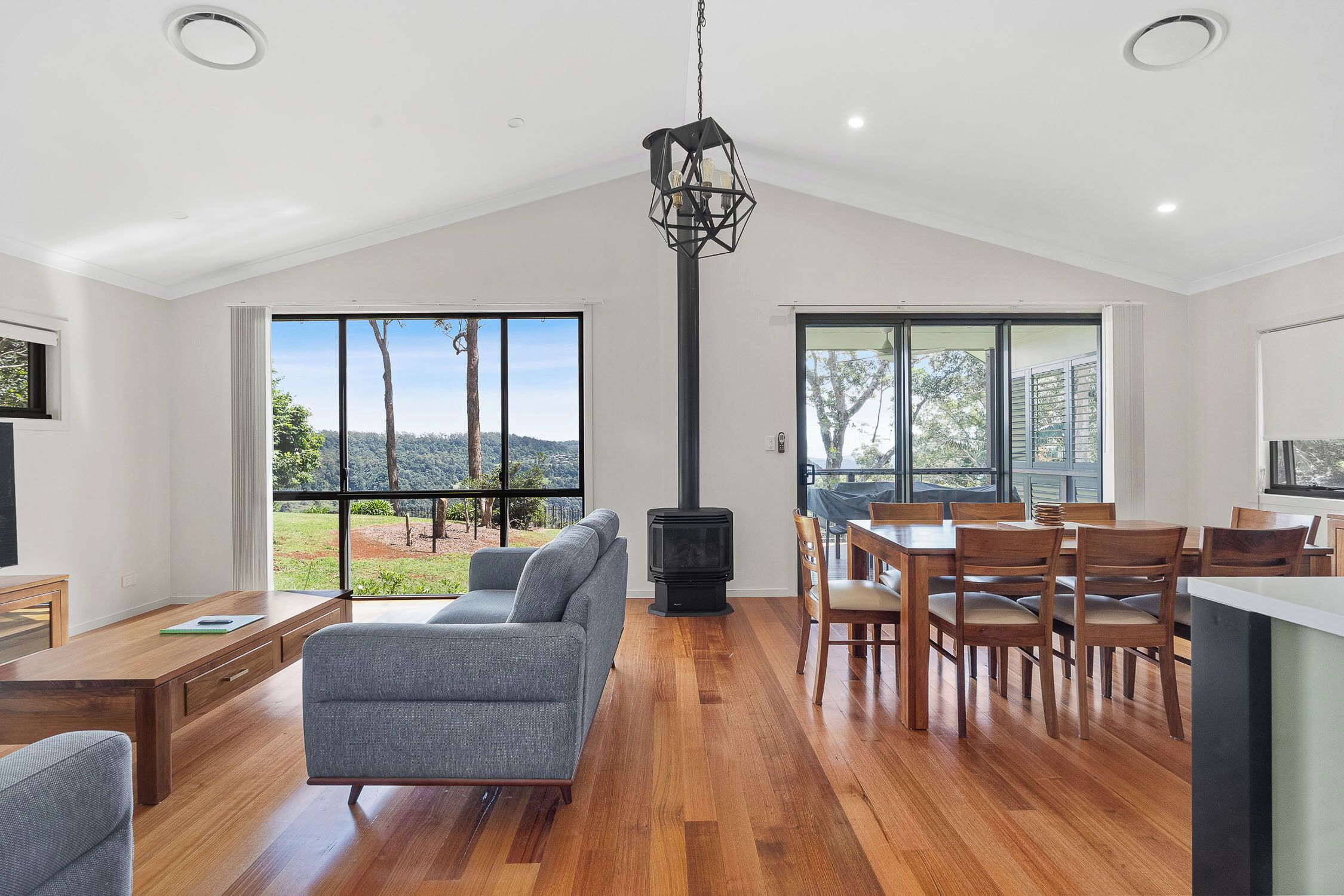 Amplia sala de estar con sofá, mesa de comedor y sillas, chimenea y ventanas grandes con vistas al exterior.