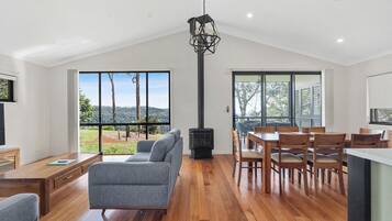Amplia sala de estar con sofá, mesa de comedor y sillas, chimenea y ventanas grandes con vistas al exterior.
