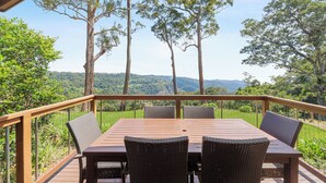 Une terrasse en bois avec une table et des chaises, offrant une vue sur un paysage luxuriant, avec des arbres et des collines.
