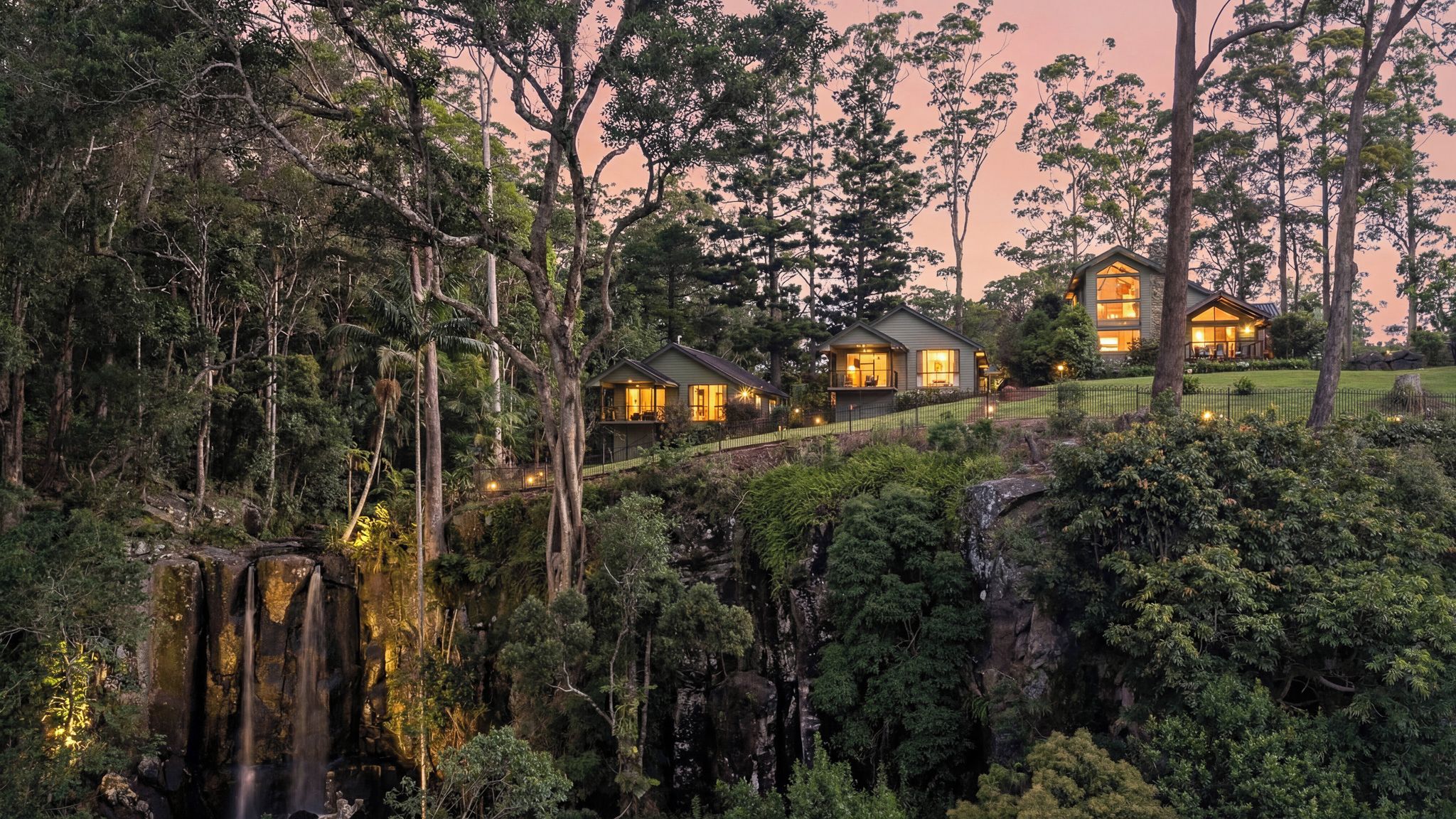 A secluded resort with multiple cabins surrounded by dense forest and a waterfall.