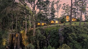 Un complexe hôtelier isolé, composé de plusieurs chalets entourés d’une forêt dense et situé près d’une cascade.