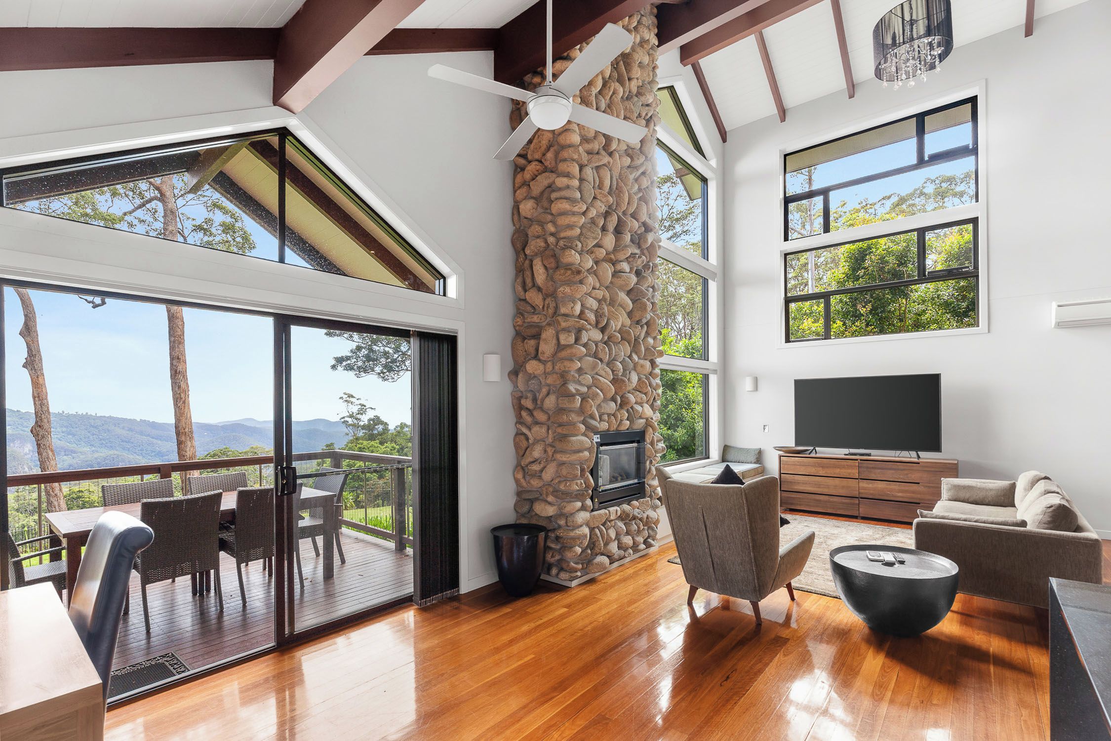 A modern living room with a stone fireplace, large windows, and a flat-screen TV.