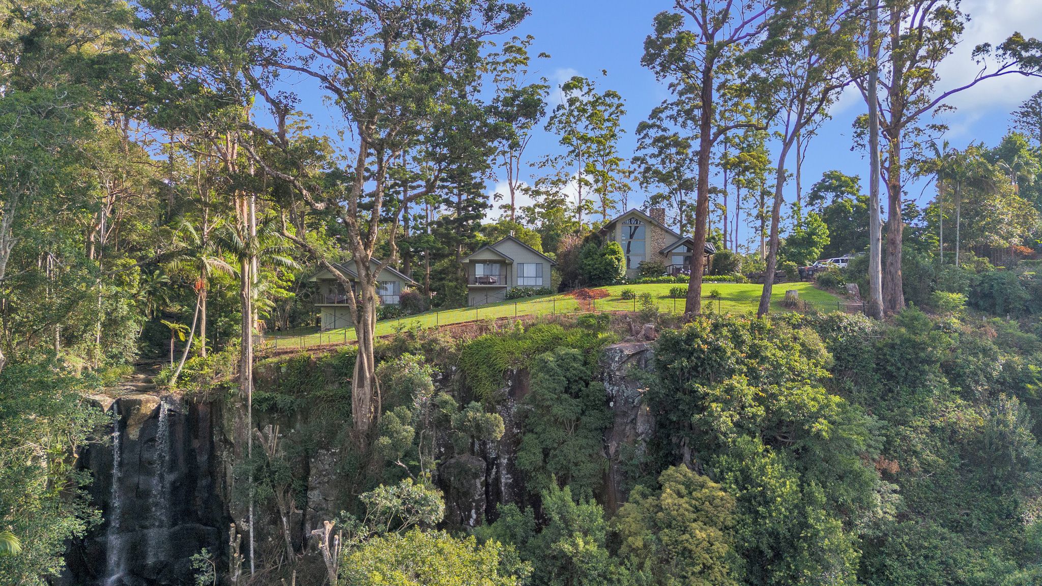 A residential area with houses on a hillside, surrounded by dense forest and a waterfall.