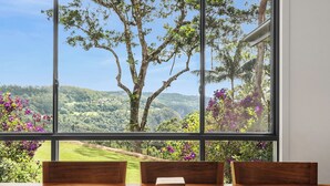 Un espace repas offrant une vue sur un paysage luxuriant grâce à de grandes fenêtres.