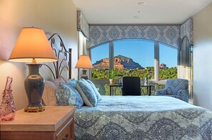 Ein Schlafzimmer mit einem Bett, zwei Lampen, einer Vase, einem Stuhl und Blick auf einen Berg und eine Stadt.