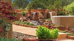 A garden with a small waterfall, surrounded by rocks and plants. - Bell Rock Haven // 3bd 3.5ba // Amazing Views (Sedona)