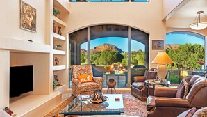 A spacious living room with a fireplace, comfortable seating, a coffee table, and a large window offering a scenic view of a mountain and forest. - Bell Rock Haven // 3bd 3.5ba // Amazing Views (Sedona)
