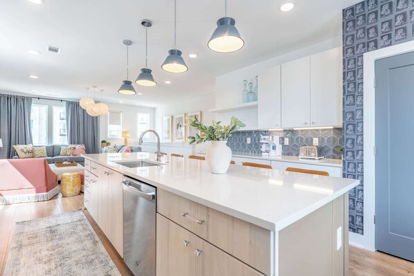 A modern kitchen with a large island, pendant lights, and a backsplash with a geometric pattern.