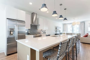 A modern kitchen with a central island, stainless steel appliances, pendant lighting, and a seating area with a sofa and bar stools. - Nashville getaway: 2 rooftop homes with hot tub & fire pit, sleeps 24 (Nashville)