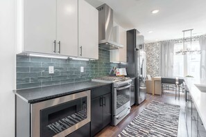 Une cuisine moderne dotée d’appareils électroménagers en acier inoxydable, d’un plan de travail noir et d’un pare-feu décoratif.
