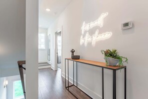 A modern hallway with a neon sign, a console table with a plant, and a digital thermostat.