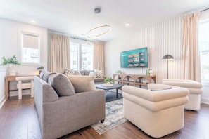 Un salon moderne avec un canapé, des fauteuils, une table basse et un téléviseur fixé au mur.