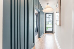 Un couloir avec une porte de couleur foncée, un plancher de couleur claire et un luminaire au plafond.