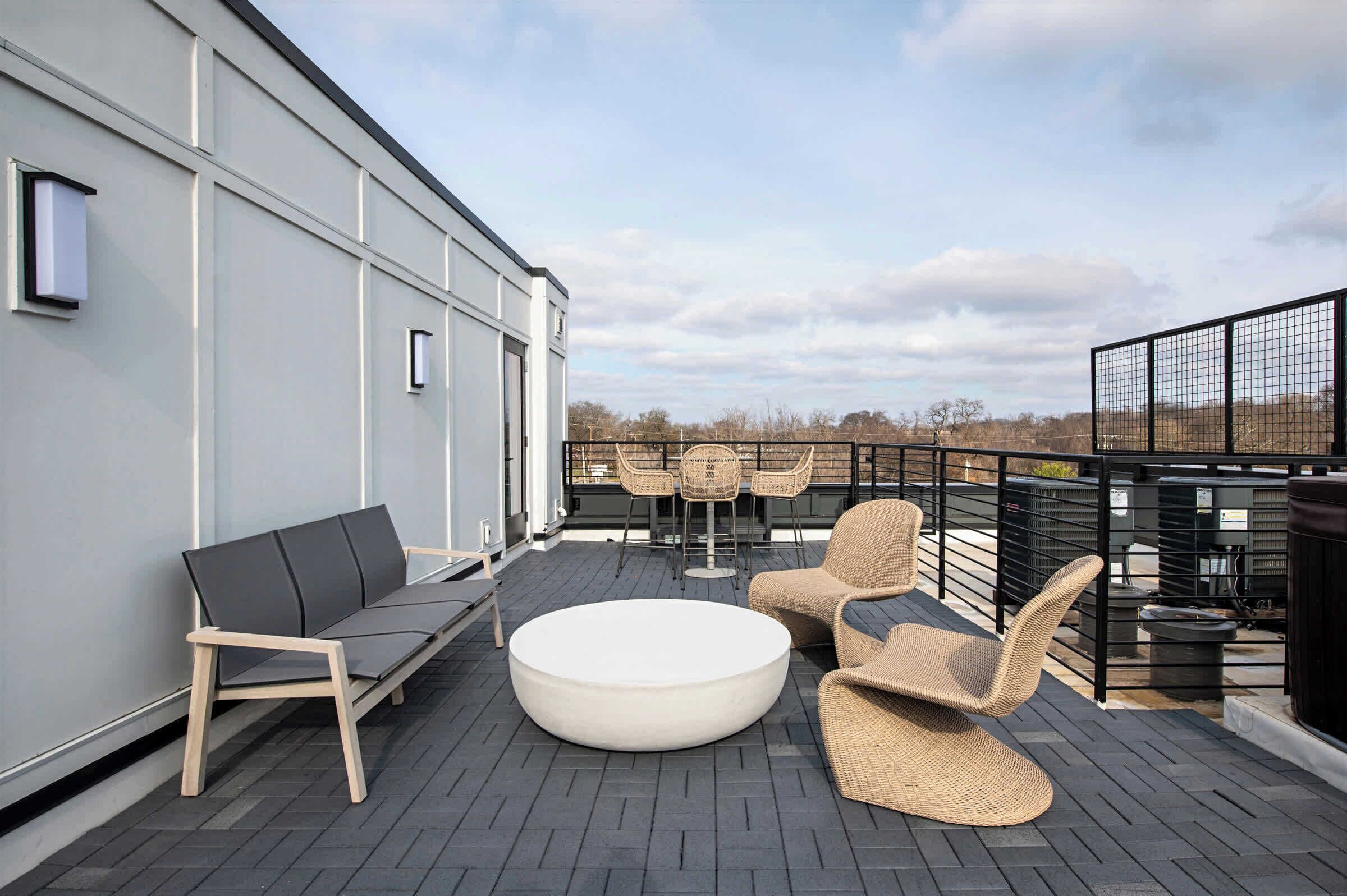A rooftop terrace with a sofa, round table, and wicker chairs.