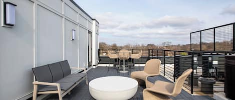 Une terrasse sur le toit, aménagée avec un canapé, une table ronde et des chaises en osier.