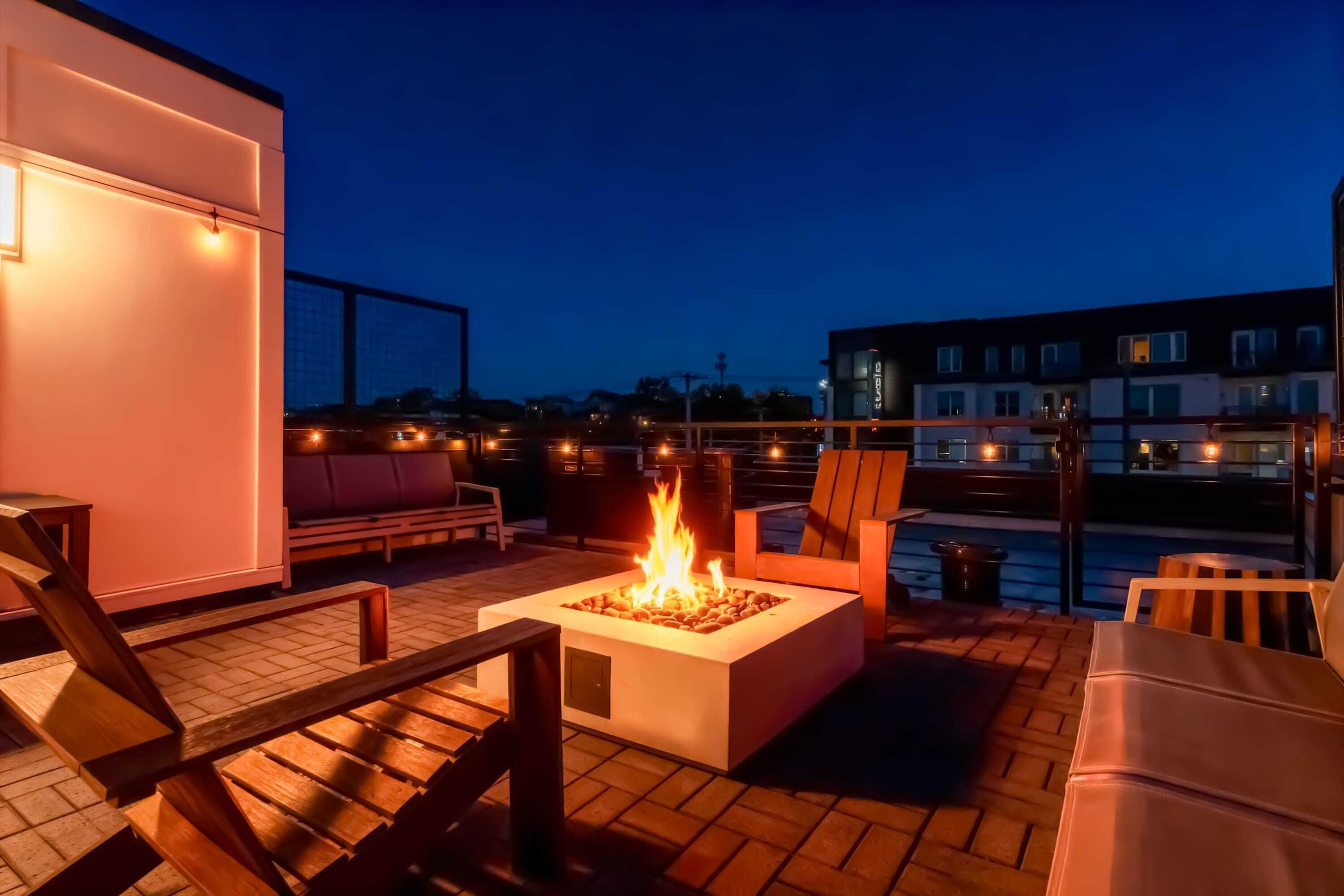 A rooftop terrace with a fire pit, seating area, and city views at dusk.