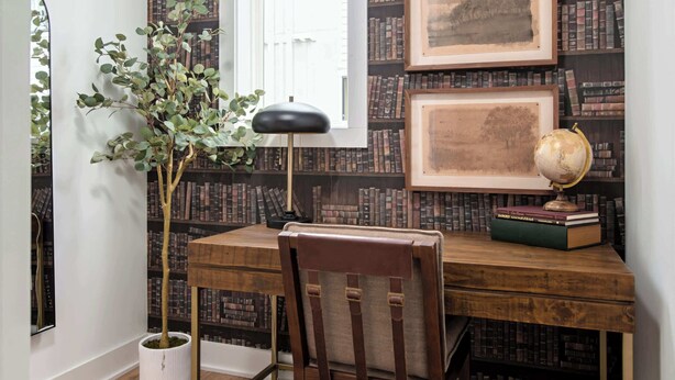 A study room with a wooden desk, a chair, a globe, framed pictures, and a bookshelf against the wall.
