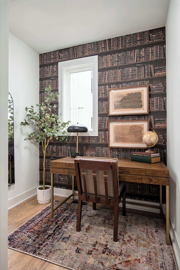 A study room with a wooden desk, a chair, a globe, framed pictures, and a bookshelf against the wall.