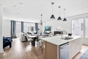 Une cuisine moderne avec un îlot central, un coin repas avec un canapé et des chaises, et un salon équipé d’un téléviseur.
