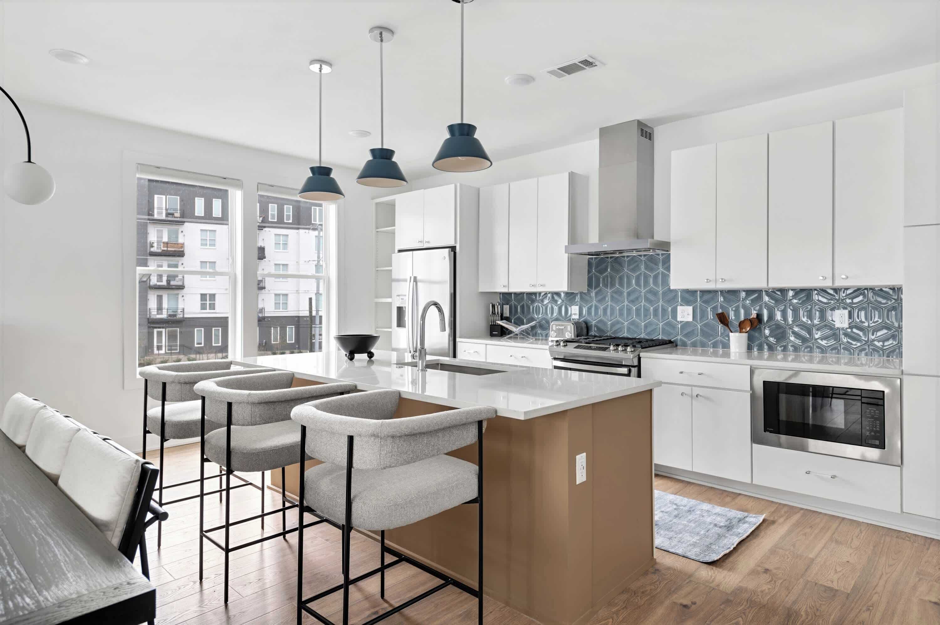 A modern kitchen with white cabinets, a central island, and a view of residential buildings.