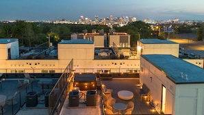 A rooftop terrace with outdoor seating, air conditioning units, and a city skyline view in the background.