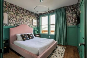 Une chambre à coucher avec un papier peint à motifs floraux, un lit rose et une fenêtre avec des rideaux.