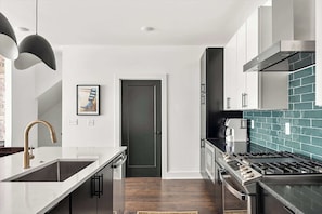 A modern kitchen with a stainless steel stove, a white countertop, and a dark wooden floor.