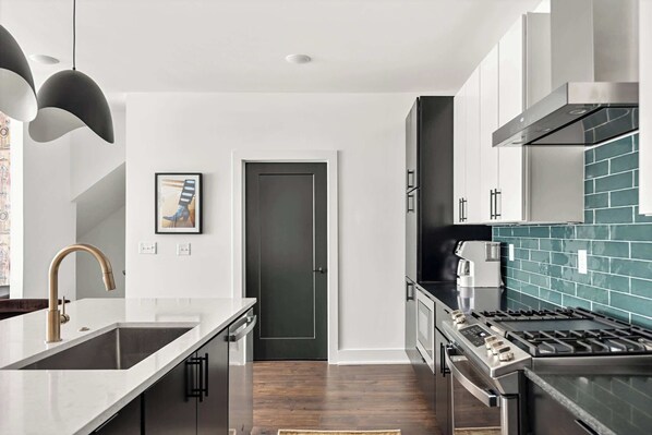 A modern kitchen with a stainless steel stove, a white countertop, and a dark wooden floor.