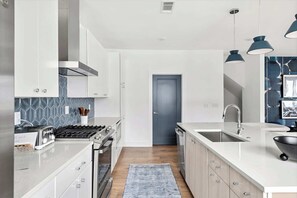 Una cocina moderna con armarios blancos, estufa a gas, lavamanos y luces colgantes.