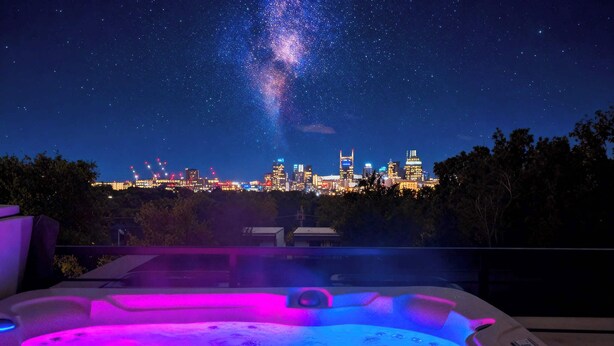 Una vasca idromassaggio con lo skyline cittadino e la Via Lattea sullo sfondo.