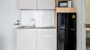 Una cocina compacta con armarios blancos, un refrigerador negro, un microondas y un lavamanos.