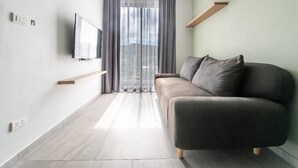 Una sala de estar moderna con un sofá, un televisor montado en la pared y un amplio ventanal con cortinas.