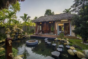 Um edifício com telhado de palha, piscina e pedras para pisar.