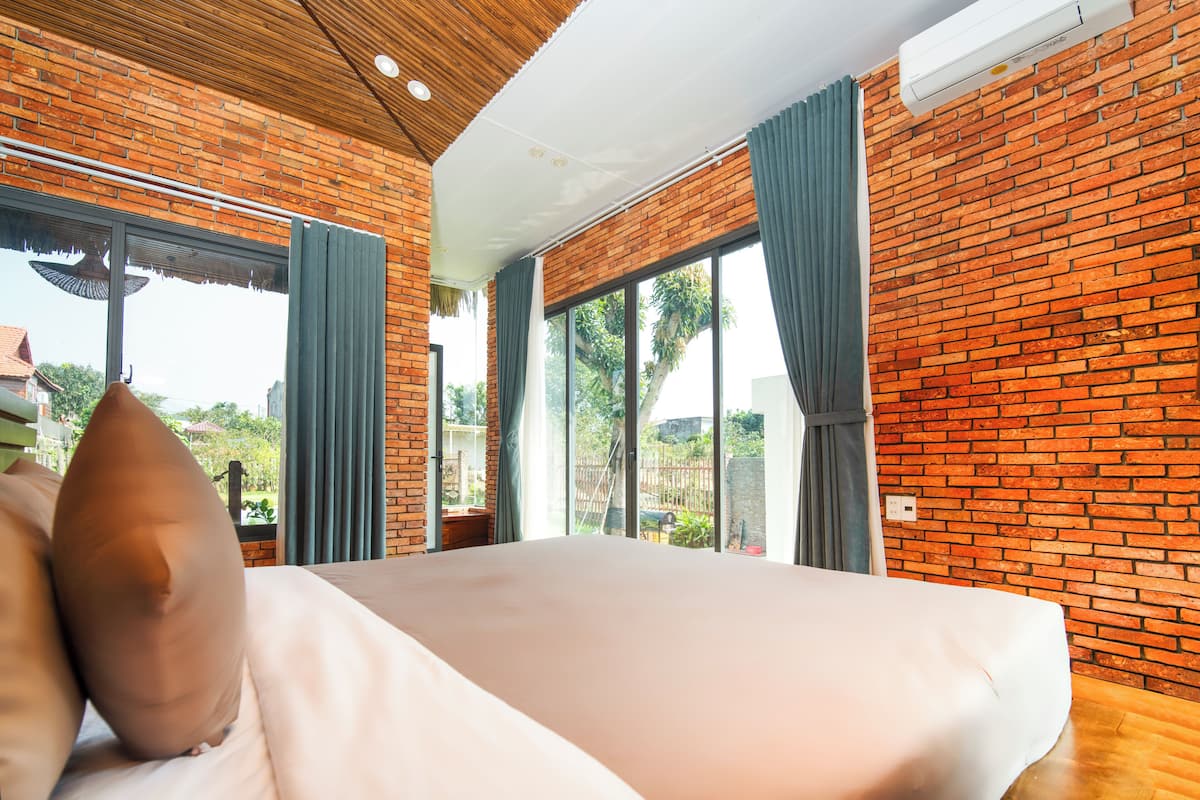 A bedroom with a large bed, brick walls, and large windows with curtains.