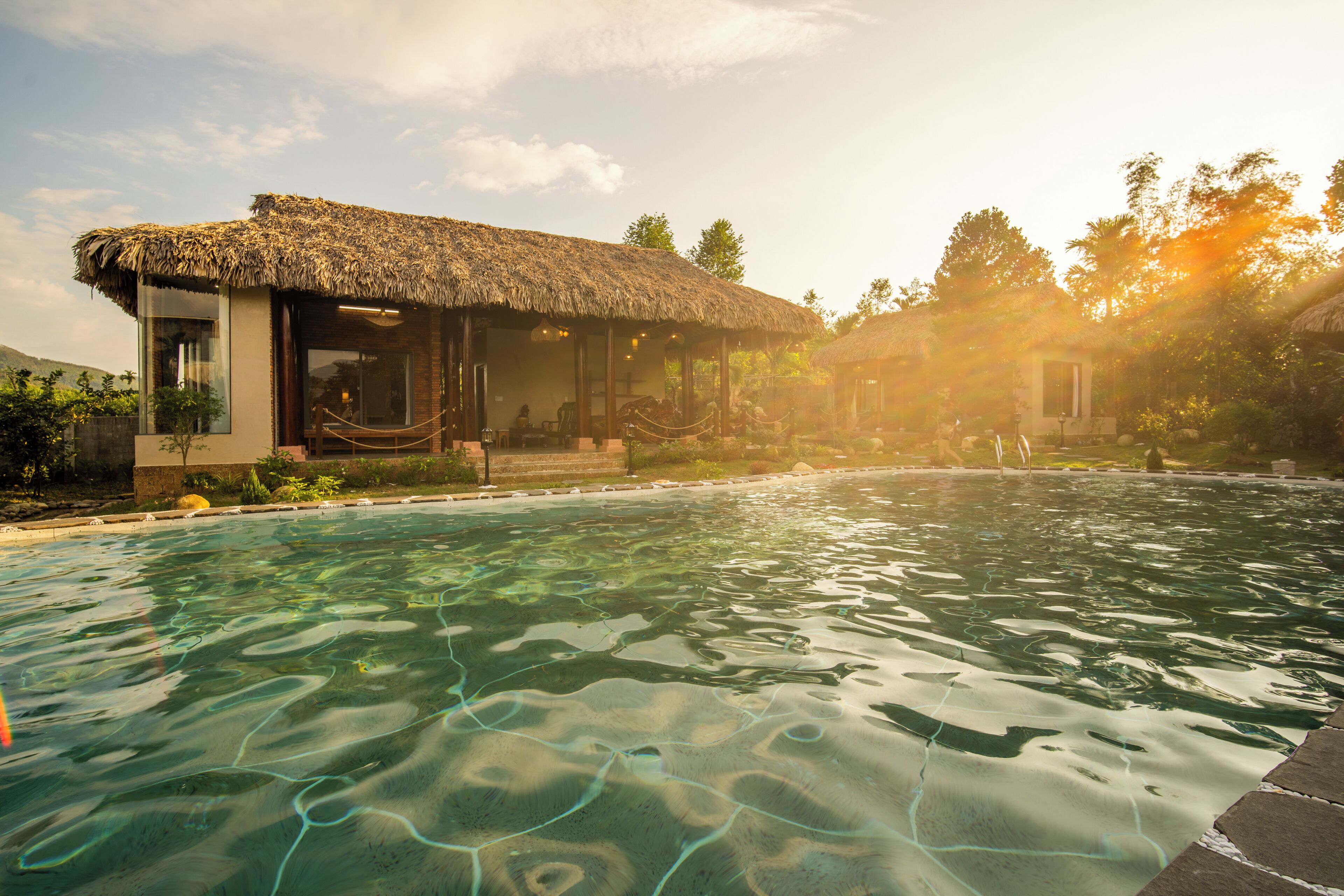 A pool with clear water, surrounded by a building with a thatched roof and a glass enclosure.