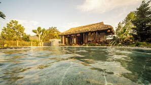 A pool with clear water, a thatched-roof building, and surrounding greenery. - Lá Retreat (Da Nang)