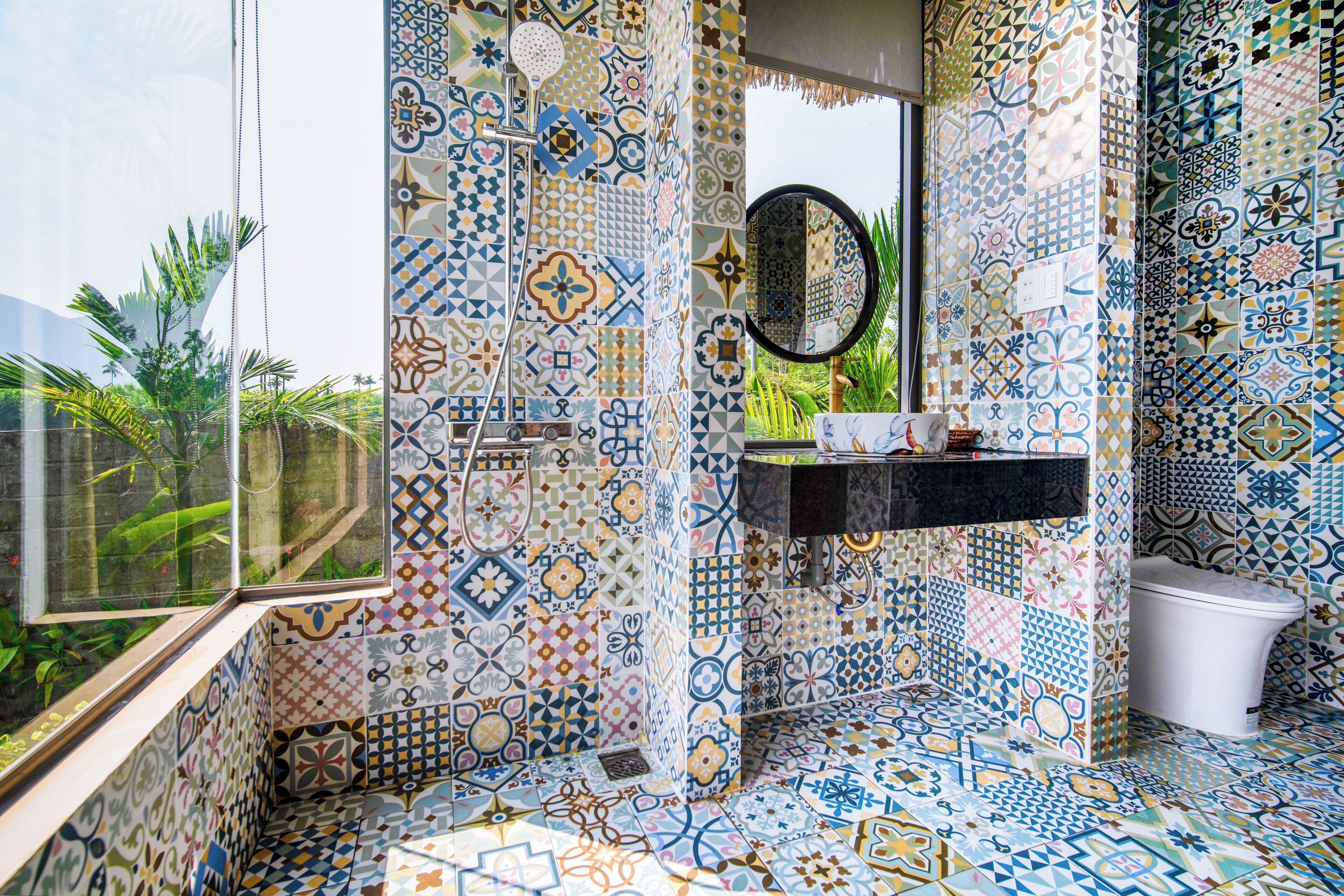 A bathroom with a variety of colorful tiles, a black sink, a mirror, and a white toilet.