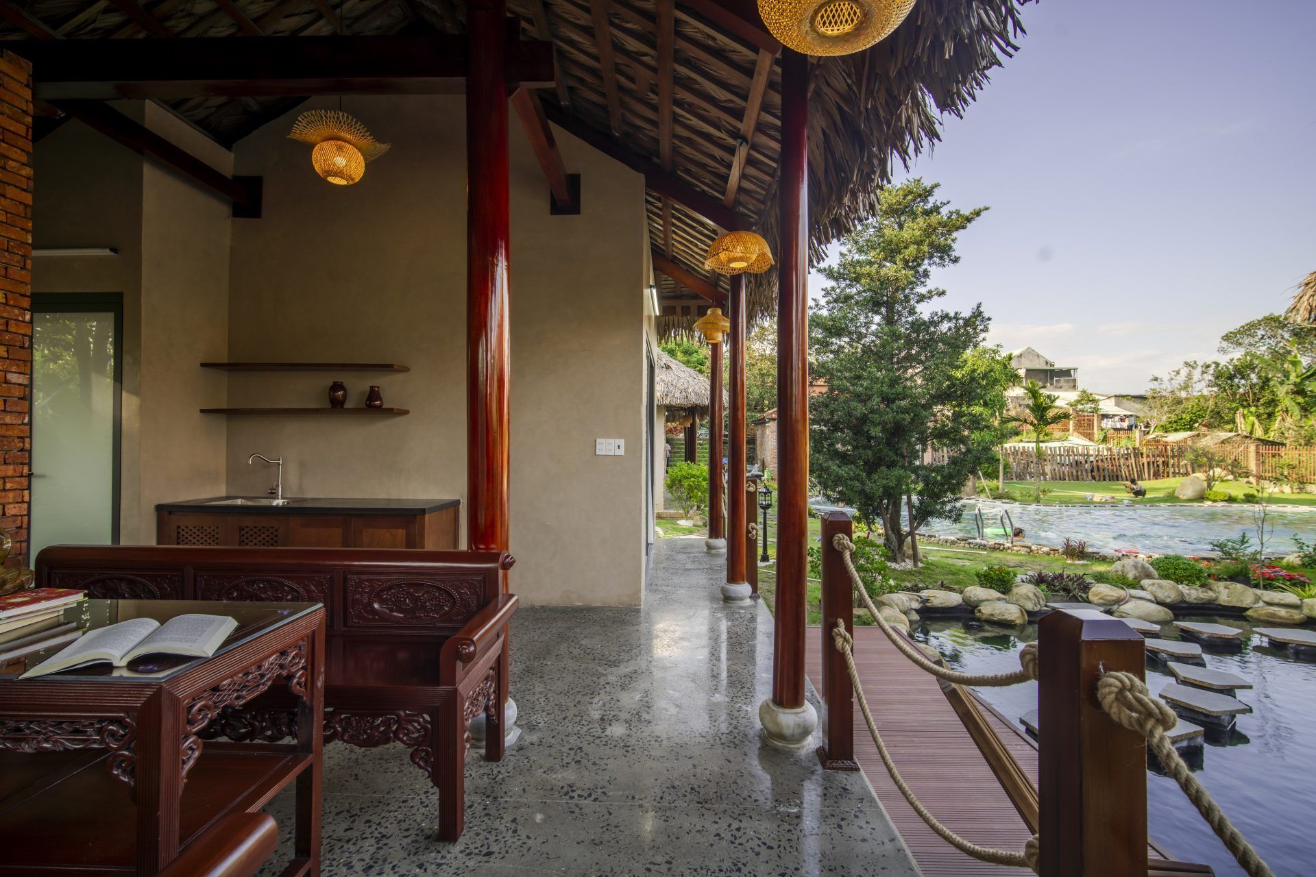 A traditional wooden structure with a thatched roof, a wooden bench, and a view of a river and garden.