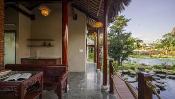 A traditional wooden structure with a thatched roof, a wooden bench, and a view of a river and garden.