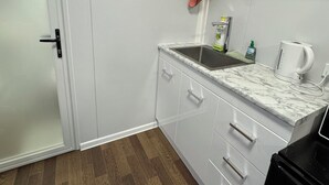 A compact kitchen with white cabinets, a marble countertop, a sink, and a black stove.