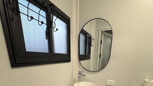 A compact bathroom with a white sink, a round mirror, a toilet, and a window with a black frame.