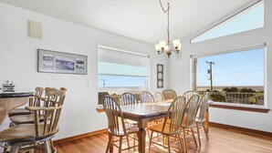 Un coin repas avec une table et des chaises en bois, de grandes fenêtres équipées de stores et un lustre.