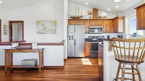 Une cuisine moderne avec des meubles en bois, des appareils en acier inoxydable et un îlot central en bois doté d’un tabouret.