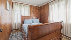 Quarto com painéis de madeira, cama, cortinas e ventilador de teto.