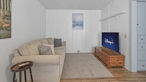 Uma sala de estar com um sofá bege, um móvel de televisão de madeira e um quadro na parede.