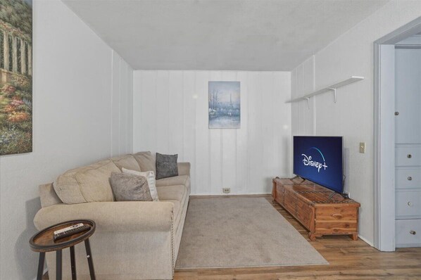 A living room with a beige sofa, a wooden TV stand, and a painting on the wall.