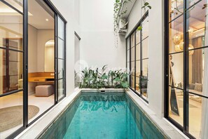 Una piscina interna moderna con pareti in vetro, circondata da piante e mobili.